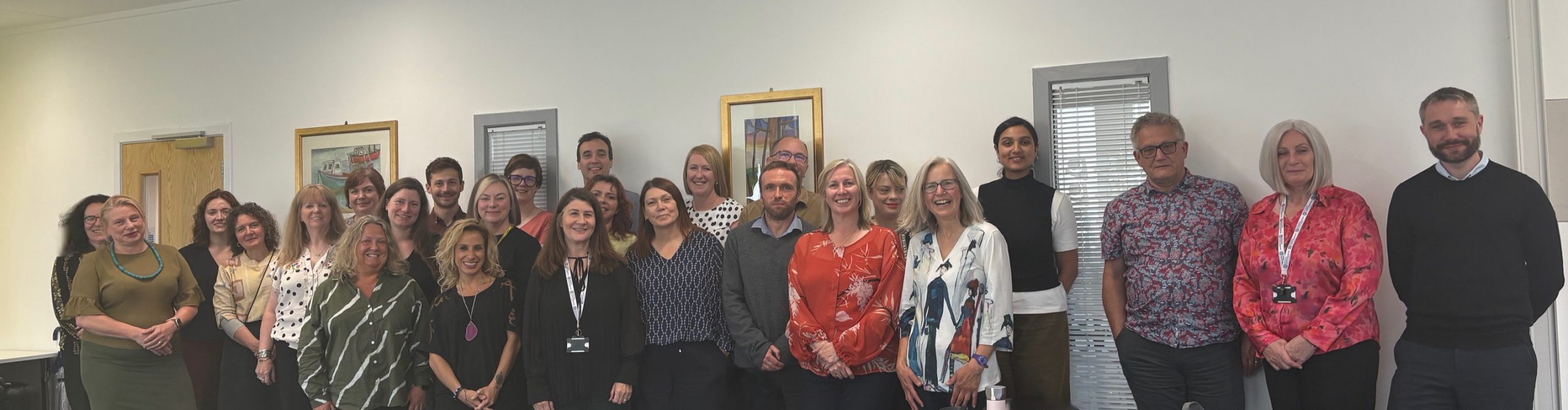 Group of people 26 people standing in a conference room.